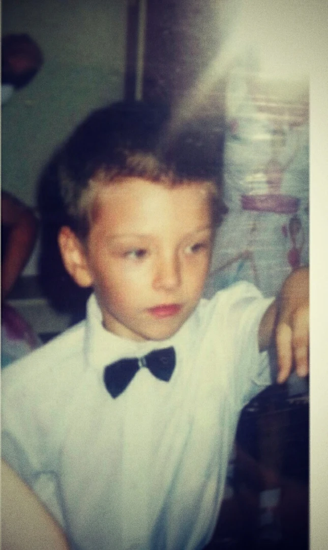 Andrei as a small boy in a white shirt and a black bow tie, in a snapshot faded with age